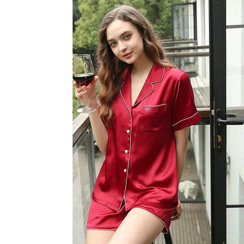 Woman in red satin pajama set holding a glass of wine on a balcony.