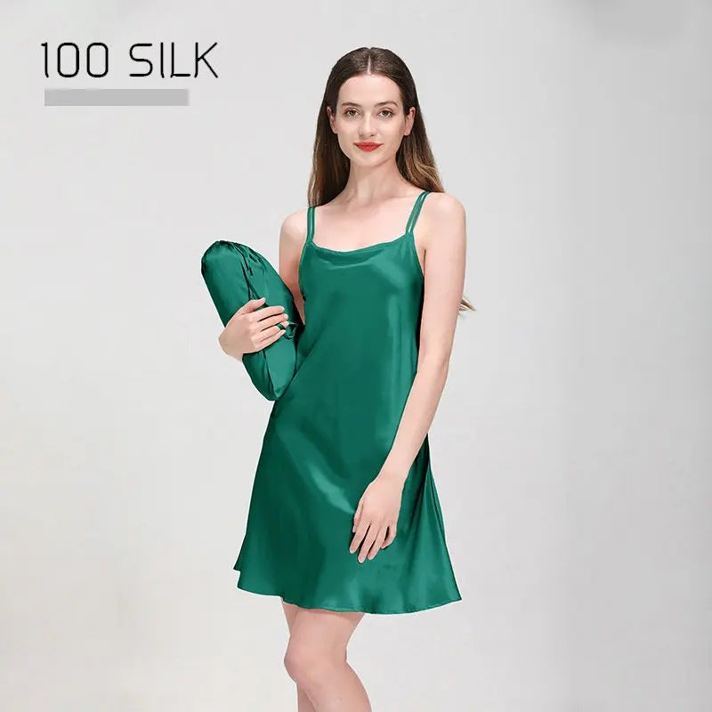 Woman wearing a green silk slip dress holding a matching bag on a light gray background.