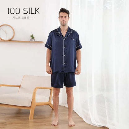 Man wearing navy silk pajamas in a room with a white curtain and wooden chair.