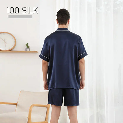 Man wearing navy silk pajamas in a room with a clock and plant on a shelf.