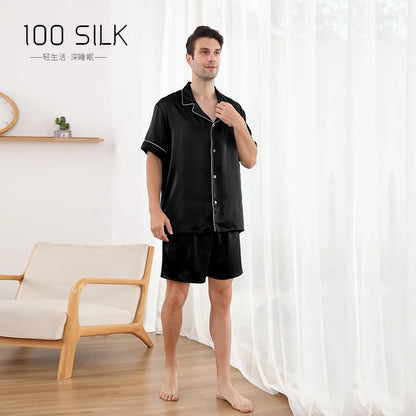 Man wearing black silk pajamas standing in a room with white curtains and a wooden chair.