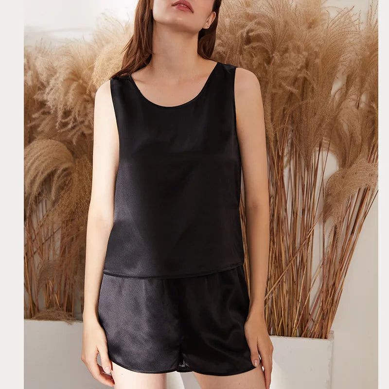 Person wearing a black satin tank top and shorts set against a neutral background with decorative plants.