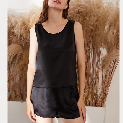 Person wearing a black satin tank top and shorts set against a neutral background with decorative plants.