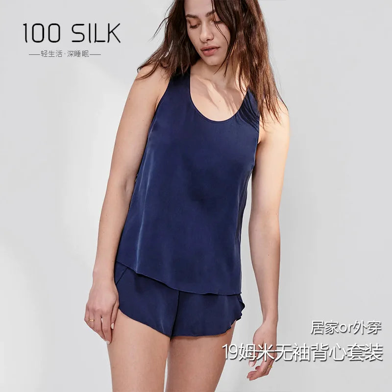 Woman wearing a navy blue silk tank top and shorts set on a light gray background with '100 SILK' branding.