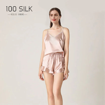 Woman wearing a pink satin pajama set with '100 Silk' branding on a light gray background.