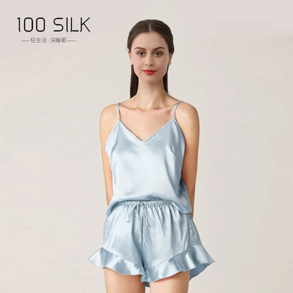 Woman wearing a light blue silk pajama set with '100 Silk' branding on a plain background.