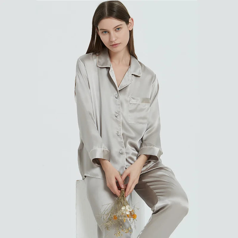 Woman wearing a light gray satin pajama set holding dried flowers on a white background