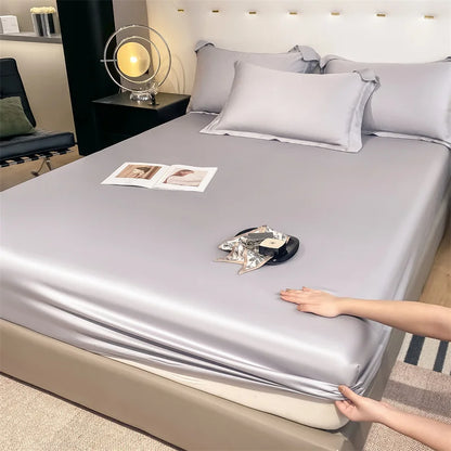 Person adjusting a silver satin sheet on a bed in a bedroom setting.