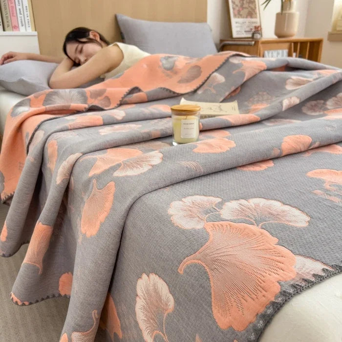 Woman lying on a bed with a floral-patterned gray and pink blanket, surrounded by books and a candle.