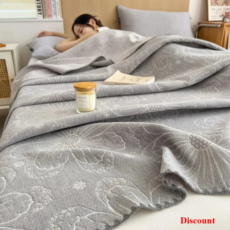 Gray floral-patterned comforter on a bed with a candle and book, indicating a relaxing setting.