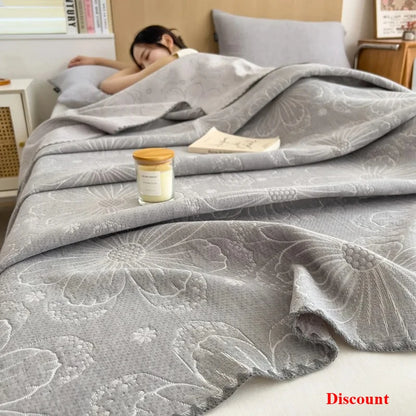 Gray floral-patterned comforter on a bed with a candle and book, indicating a relaxing setting.