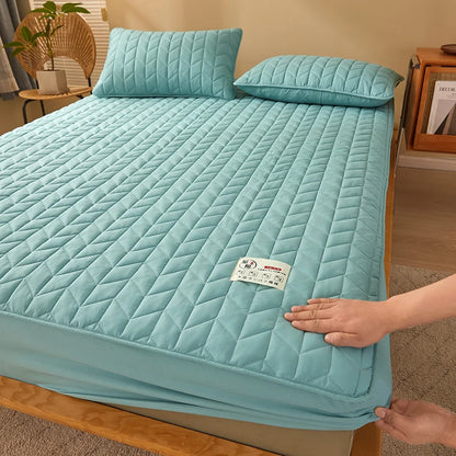 Person adjusting a light blue quilted mattress cover on a bed in a room.