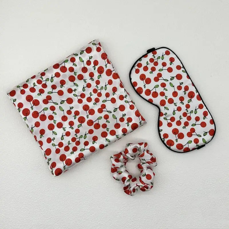 Set of cherry-patterned pouch, eye mask, and scrunchie on a white background