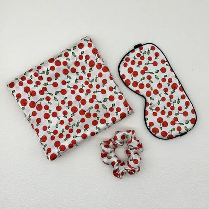 Set of cherry-patterned pouch, eye mask, and scrunchie on a white background