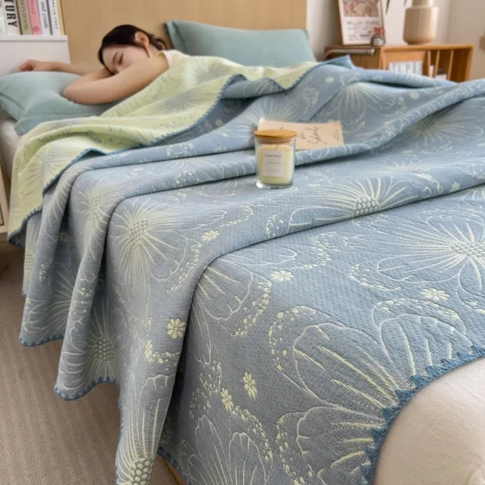 Woman lying on a bed with a floral-patterned blue blanket, candle, and books in the background.