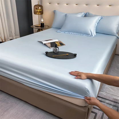 Person stretching a light blue satin sheet over a bed in a bedroom setting.