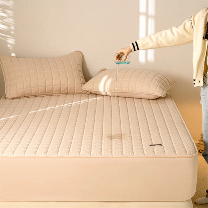 Beige quilted mattress cover on a bed with a person holding a glass of water.