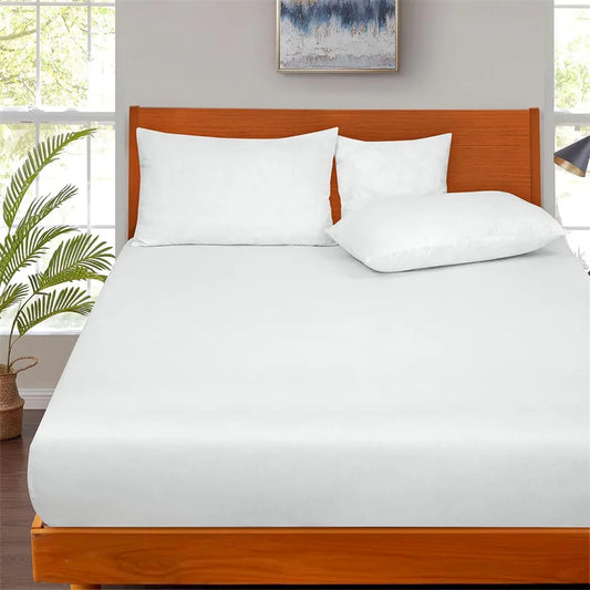 Bed with white bedding and wooden headboard in a room with windows and plants.