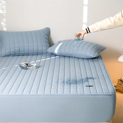 Light blue quilted mattress cover on a bed with a hand holding a pillow.