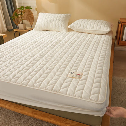 Quilted mattress cover on a bed in a room with a plant and window.