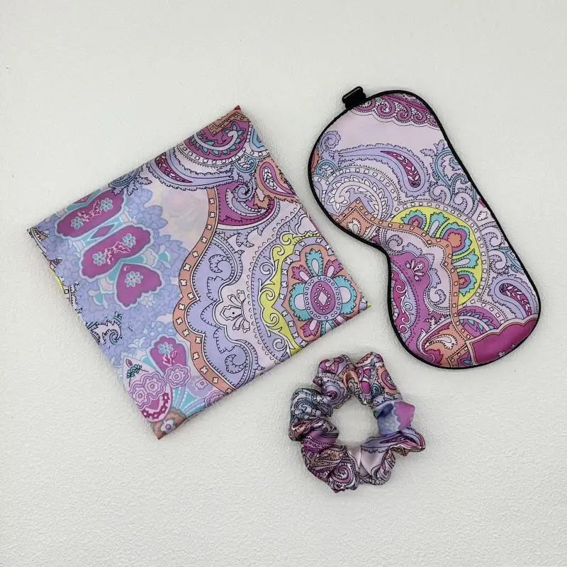 Set of paisley-patterned pouch, eye mask, and scrunchie on a light gray background